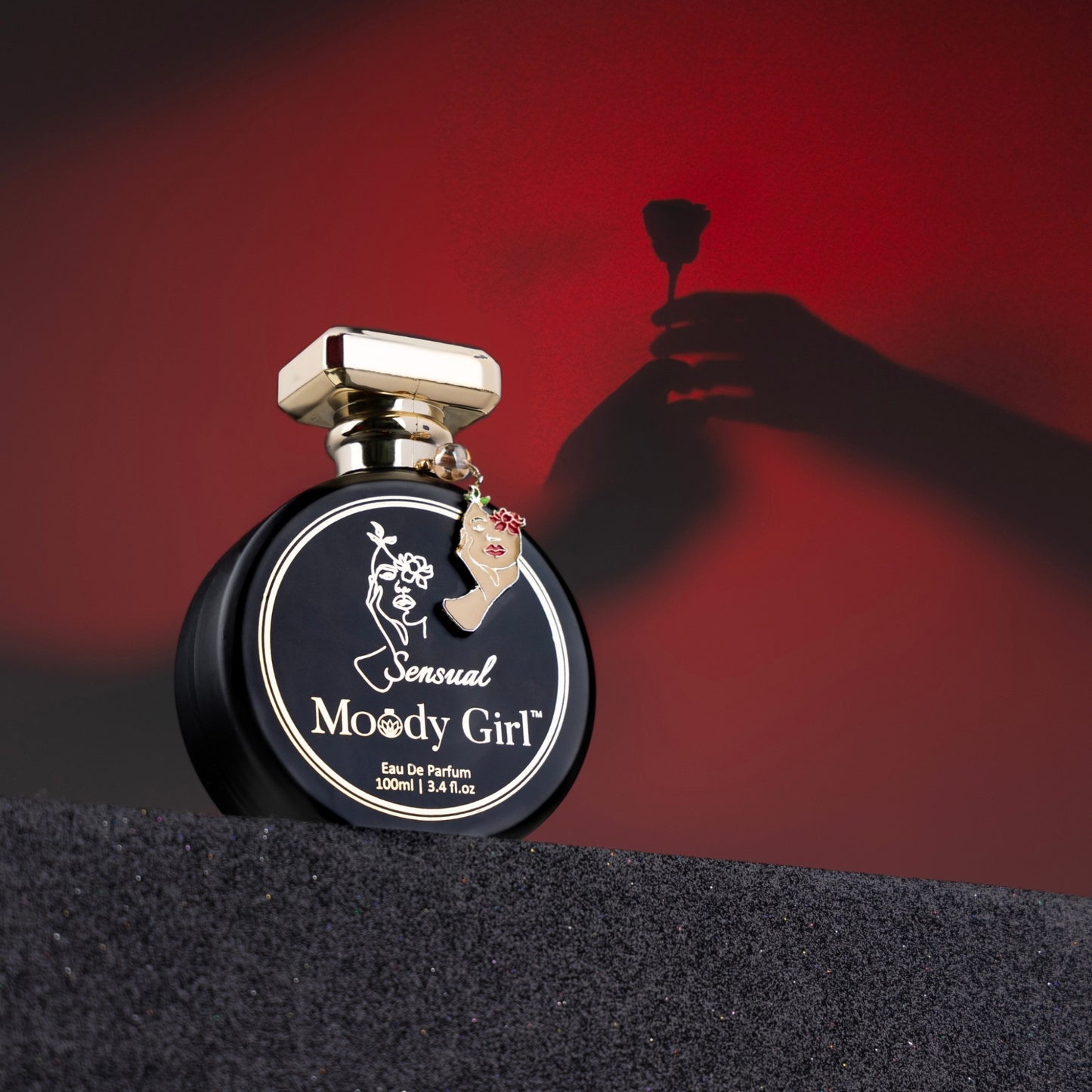 Perfume bottle labeled 'Sensual Moody Girl' with a hand holding a perfume sprayer against a red background.
