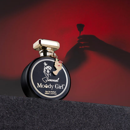 Perfume bottle labeled 'Sensual Moody Girl' with a hand holding a perfume sprayer against a red background.